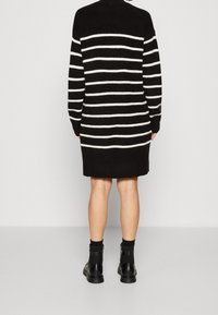 Abito a maglia a strisce bianco e nero con maniche lunghe e scollo a costine, indossato con stivali alla caviglia neri e pelle visibile sopra il ginocchio.