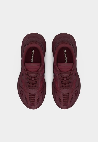 Ζευγάρι σκούρων κόκκινων αθλητικών παπουτσιών Emporio Armani με λεπτομέρειες από δίχτυ και δέρμα, με δεμένα κορδόνια, φωτογραφημένα από πάνω σε απλό φόντο.
