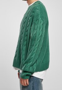 Pull vert tricoté avec un motif en torsades, coupe oversize, poignets et ourlet côtelés, texture douce et col rond.