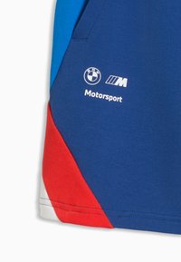 Tissu bleu, rouge et blanc avec le logo BMW Motorsport imprimé en blanc sur la partie bleue du vêtement.