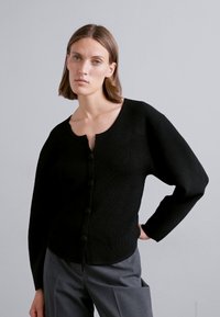 Black ribbed cardigan with a round neckline, long sleeves, and five matching buttons down the front. Smooth texture, fitted shape.