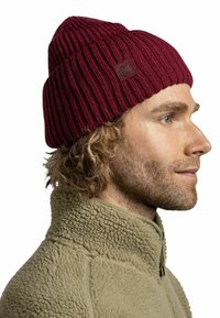Maroon knitted beanie with a ribbed design, featuring a small brown logo patch. The fabric appears soft and textured.