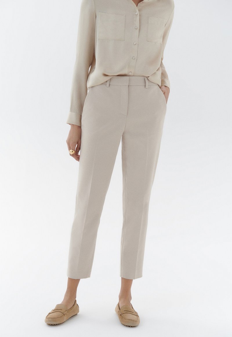 Pantalons beiges ajustés avec une coupe slim, taille haute et deux poches avant. Associés à une chemise boutonnée beige clair et des mocassins beiges.