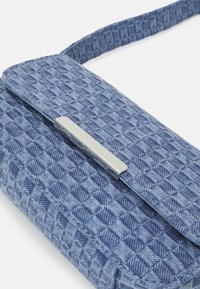 Niebieska pleciona torebka o geometrycznej fakturze, zapięcie z srebrnym elementem metalowym. Projekt jest kompaktowy, posiada pasek na ramię.