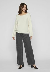 Pull crème, ample avec un large décolleté ; associé à un jean large taille haute gris foncé ; chaussures à talons carrés noires.