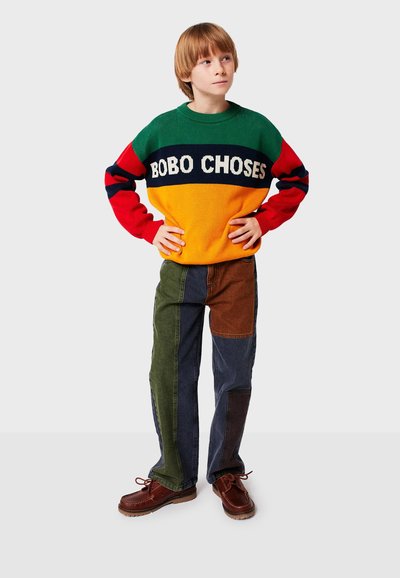 Suéter de punto con secciones en verde, rojo y naranja, con el texto "BOBO CHOSES". Pantalones de mezclilla tipo patchwork en verde, marrón, azul y azul oscuro. Calzado marrón.