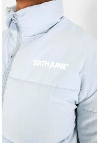 Giacca puffer azzurro chiaro con colletto alto e zip frontale. Il nome del brand "SIXTH JUNE" è stampato in bianco sul petto.