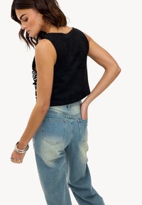 Zwarte crop top van suede met een ronde halslijn en mouwloos ontwerp, gecombineerd met lichtblauwe denim jeans met een relaxed pasvorm.