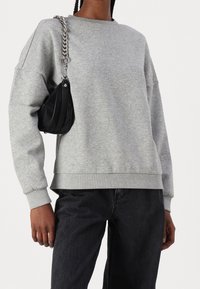 Grå tröja med långa ärmar och ribbade muddar, som matchas med svart väska med en silverfärgad kedjesnobb. Avslappnad passform och mjuk textur.