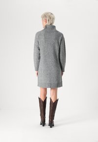 Robe pull grise en tricot avec un col montant, motif texturé et ourlet côtelé, associée à des bottes de cowboy en cuir marron avec des tiges pointues.