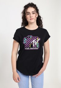 Zwarte katoenen t-shirt met een kleurraf MTV-afbeelding met een dambordpatroon, opgerolde mouwen en een afgeronde zoom. Blauwe jeans gedragen.