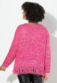 Rosa gestrickter Pullover mit lockerem Sitz, der einen fransigen Saum und lange Ärmel aufweist. Die Textur ist grob und weich, ideal zum Übereinandertragen.