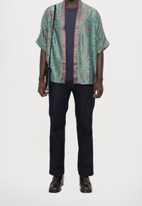 Kimono-inspireret skjorte i turkis med blomstermønster, kantet af en struktureret rød accent. Kombineret med mørke jeans og sorte loafers.