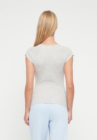 Εφαρμοστό γκρι κοντομάνικο μπλουζάκι με στρογγυλή λαιμόκοψη, λεία υφή και ελαφρώς καμπύλη ραφή, συνδυασμένο με ανοιχτό μπλε παντελόνι.