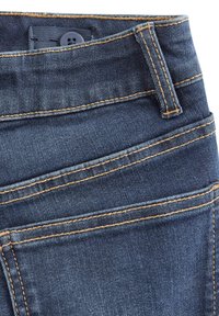 Mørkeblå denimjeans med en jevn tekstur, synlig orange søm, to frontlommer og en knappelukking i midjen.