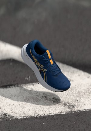 Scarpa da atleta blu con tomaia perforata, dettagli gialli e suola bianca. Design leggero adatto per la corsa o per un look casual.