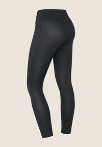 Leggings neri a vita alta con un design liscio e aderente e cuciture laterali visibili su uno sfondo neutro.