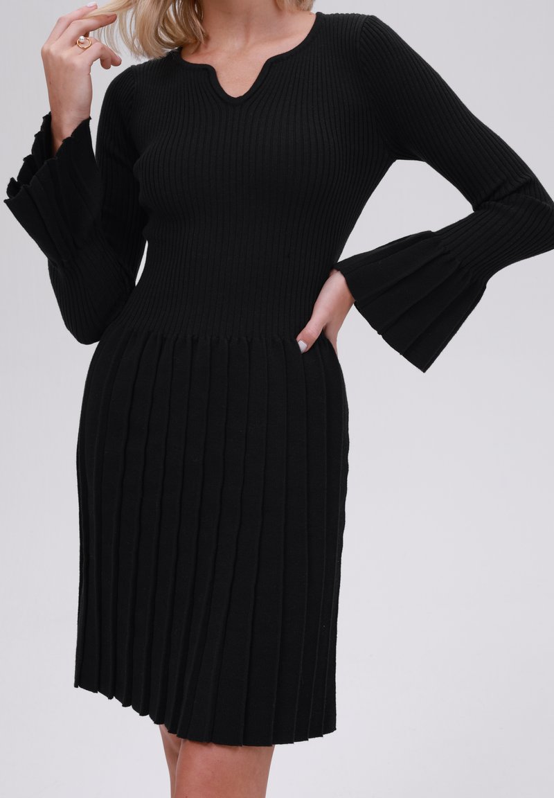 Schwarzes geripptes Strickkleid mit ausgestellten Ärmeln, V-Ausschnitt und vertikalen Falten von der Taille bis zum Saum.