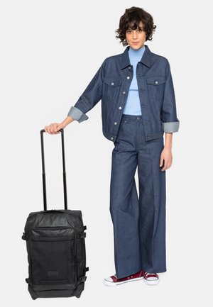 Denim jacket and wide-leg pants in dark blue worn with a light blue top and red sneakers; black rolling suitcase with multiple compartments.