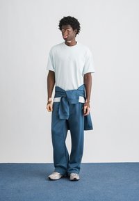 Γαλάζιο κοντομάνικο μπλουζάκι με λογότυπο, σκούρο μπλε αθλητικό παντελόνι και γκρι αθλητικά παπούτσια, με φούτερ δεμένο γύρω από τη μέση.