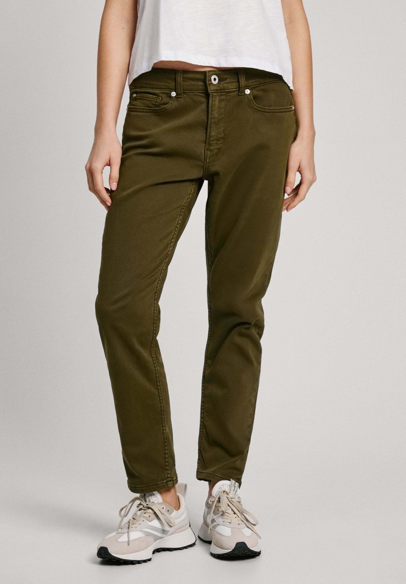 Pantalone od mješavine pamuka u maslinasto zelenoj boji s dizajnom pet džepova, zatvaračem i metalnim gumbom, kombinirani s bež i crnim sportskim cipelama.