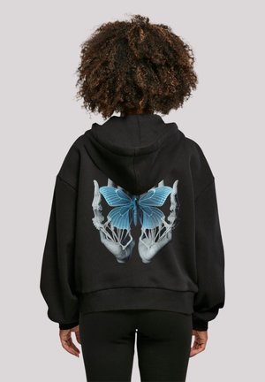 Schwarzer Kapuzenpullover mit einem großen Grafikdesign von blauen Schmetterlingsflügeln und skelettartigen Händen auf der Rückseite. Verfügt über eine Kordelzugkapuze und einen gerippten Saum.