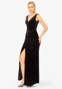 Abito in velluto nero con scollatura a V profonda, corpino arricciato e spacco alto fino alla coscia. Design senza maniche e lunghezza fino al pavimento con una texture elegante.