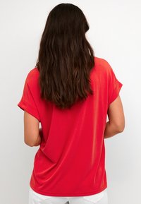 T-shirt rosso a maniche corte realizzato in tessuto morbido, con un fit rilassato e bordi arrotolati. Tessuto liscio con un design semplice.