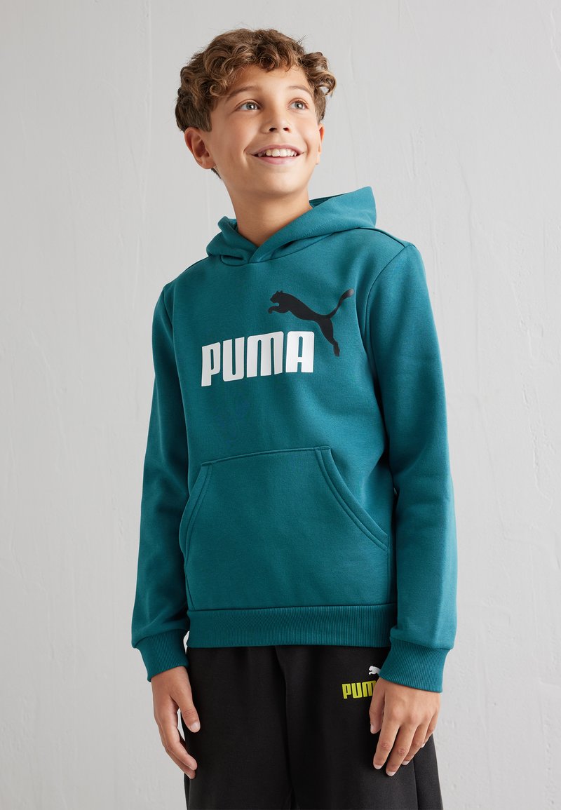 Sudadera color teal con un bolsillo canguro, que presenta un logotipo blanco de "PUMA" y un gráfico de un gato negro. Combinada con pantalones de chándal negros, resaltando los acentos de la marca.