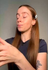 Jonge vrouw met lang, stijl haar en engel tatoeage op haar arm, ogen gesloten, met handen bewegend tegen een effen achtergrond.