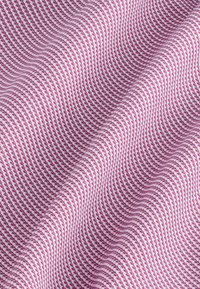 Primo piano di un tessuto pied de poule rosa e bianco con piccoli motivi intrecciati dettagliati e pieghe delicate che creano texture e profondità.