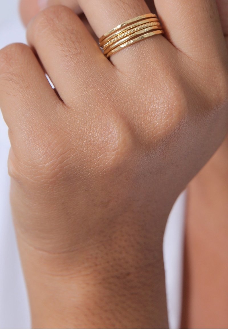 Gros plan d'une main à la carnation moyenne portant une bague en or multibandes au majeur sur un fond clair.