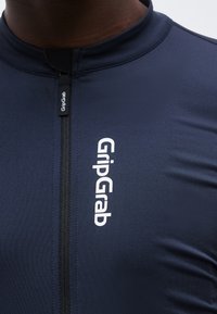 Κοντινή λήψη ενός ρούχου σε σκούρο μπλε χρώμα με φερμουάρ, που φέρει κατακόρυφο λογότυπο GripGrab στο στήθος και τραβηχτή φερμουάρ, φορεμένο από ένα άτομο.