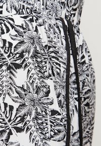 Tissu noir et blanc avec un motif de feuilles tropicales, bordé de piping noir contrastant sur les bords. Texture lisse, matériau léger.