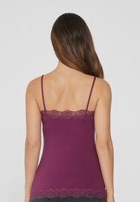 Camiseta de tirantes púrpura con encaje en el escote y el dobladillo, que presenta tirantes delgados ajustables y un diseño ajustado. Textura de tela suave.