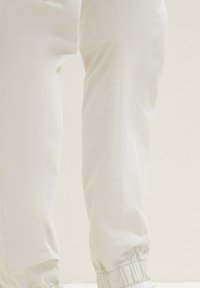 Pantalones jogger color beige claro, hechos de una tela suave, con puños elásticos, una superficie lisa y un discreto detalle de costura a lo largo de los lados.