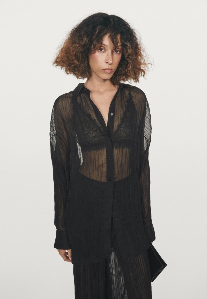 Black, sheer button-up shirt with a crinkled texture, featuring a collar and long sleeves, layered over a lace top.