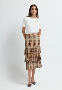 Camiseta blanca con cuello de cuentas, combinada con una falda marrón de estampado en capas que presenta tres volantes y una textura fluida.