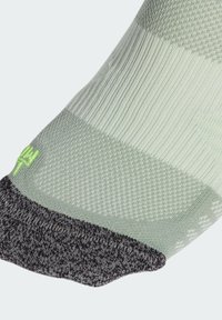 Jasnozielona skarpeta z teksturowanym wzorem, ciemnoszare wykończenie i kontrastowy zielony detal z logo. Charakteryzuje się różnymi stylami dziania oraz miękkim materiałem.