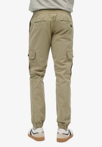 Licht khaki cargobroek met elastische manchetten, zijzakken en een relaxte pasvorm, gemaakt van een ademende stof.