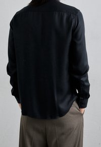Camicia di seta nera con una vestibilità rilassata, colletto appuntito e maniche lunghe, caratterizzata da un orlo curvo e polsini con bottone.