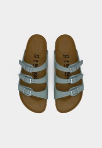 Ζευγάρι ανοιχτόχρωμα γαλάζια σανδάλια με τριπλά λουράκια, καφέ ανατομικές πέλματα και ασημένια αγκράφες, εμφανιζόμενα από επάνω σε λευκό φόντο.