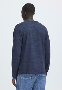 Langermet skjorte i marineblått laget av teksturert stoff, med rund hals og synlige sømmer. Brukt med lyseblå denimbukser.