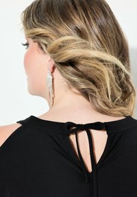 Schwarzes Oberteil mit rundem Ausschnitt und offener Rückseite, gebunden mit einer Schleife. Lange, hängende silberne Ohrringe sind sichtbar und verleihen dem Look Details.