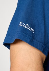 Blå bomull T-skjorte med ermer som har hvit brodert "palabon" tekst. Glatt tekstur med rett snitt og avsluttet kant.