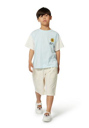 T-shirt azzurro chiaro con maniche bianche, grafica di un girasole sul petto; abbinato a pantaloni corti crema, scarpe bianche con design di tigre.