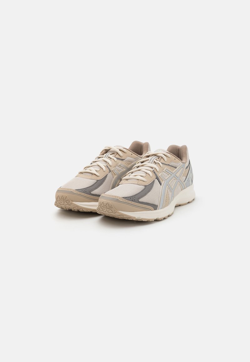Zapatillas deportivas beige con parte superior de malla y sintético, detalles grises, suela texturizada y diseño de cordones para un ajuste seguro.