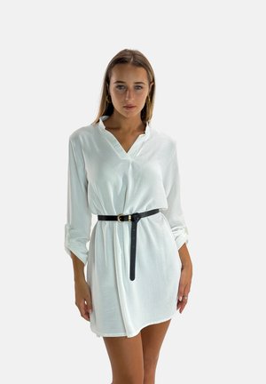 Robe blanche à col, manches longues retroussées et ceinture noire. Le tissu semble léger et légèrement texturé.