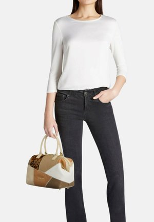 Donna che indossa una maglia bianca a maniche tre quarti e jeans neri, che tiene una borsa patchwork marrone e beige con dettaglio leopardato.