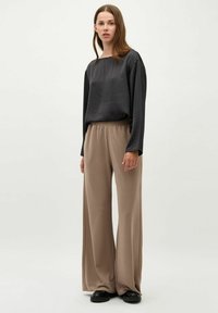 Løs pasformet mørkegrå langærmet top kombineret med beige bredbenede bukser. Blødt stof med elastisk talje. Sorte sko fuldender outfitet.